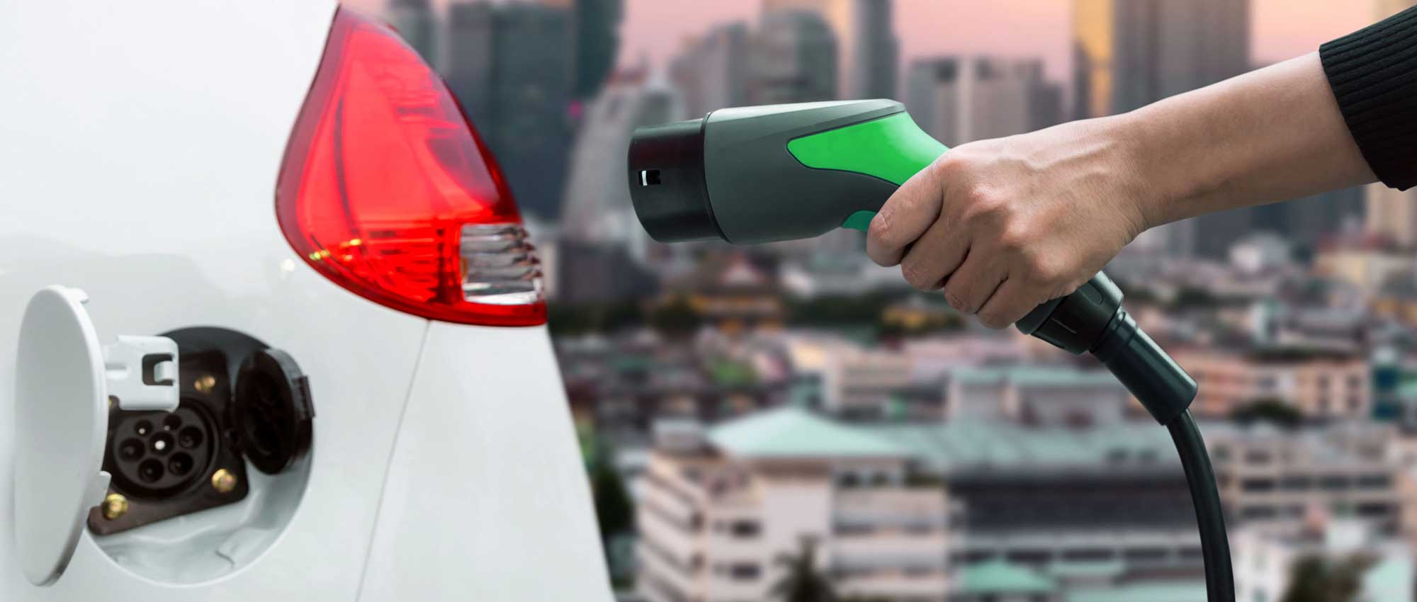 Imagen de una persona cargando un coche eléctrico con la ciudad de fondo